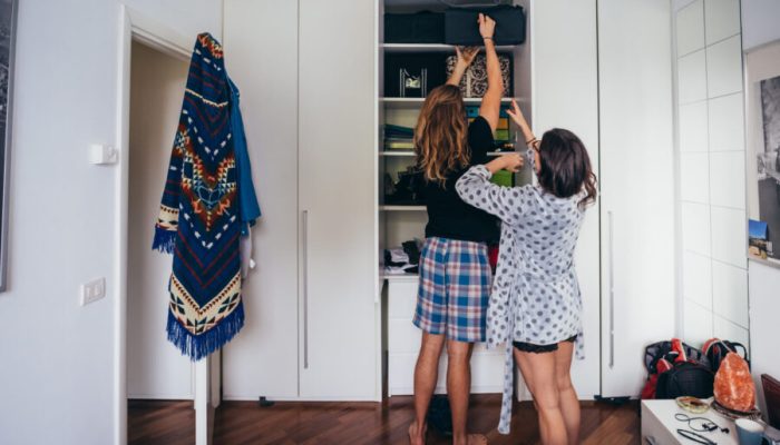 Young beautiful couple indoor bedroom trying to reach the top of the wardrobe - searching, putting in order concept